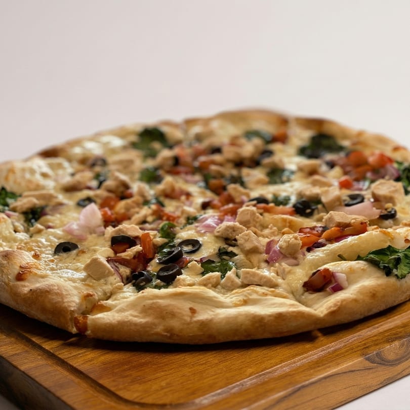 A chicken pizza with black olives, red onions, and spinach on a wooden board.